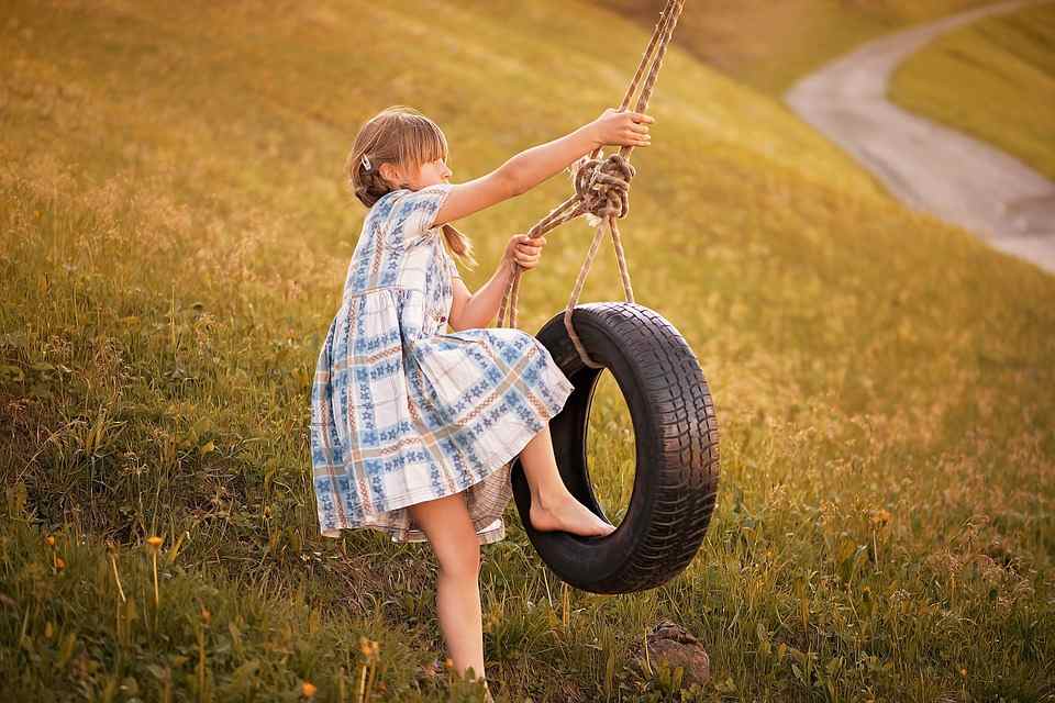 girl in plaid dress playing on tire swing