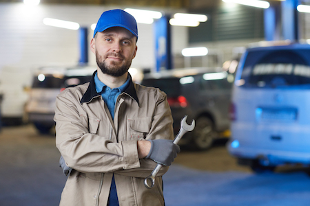 mechanic standing in an auto shop while holding a tool
